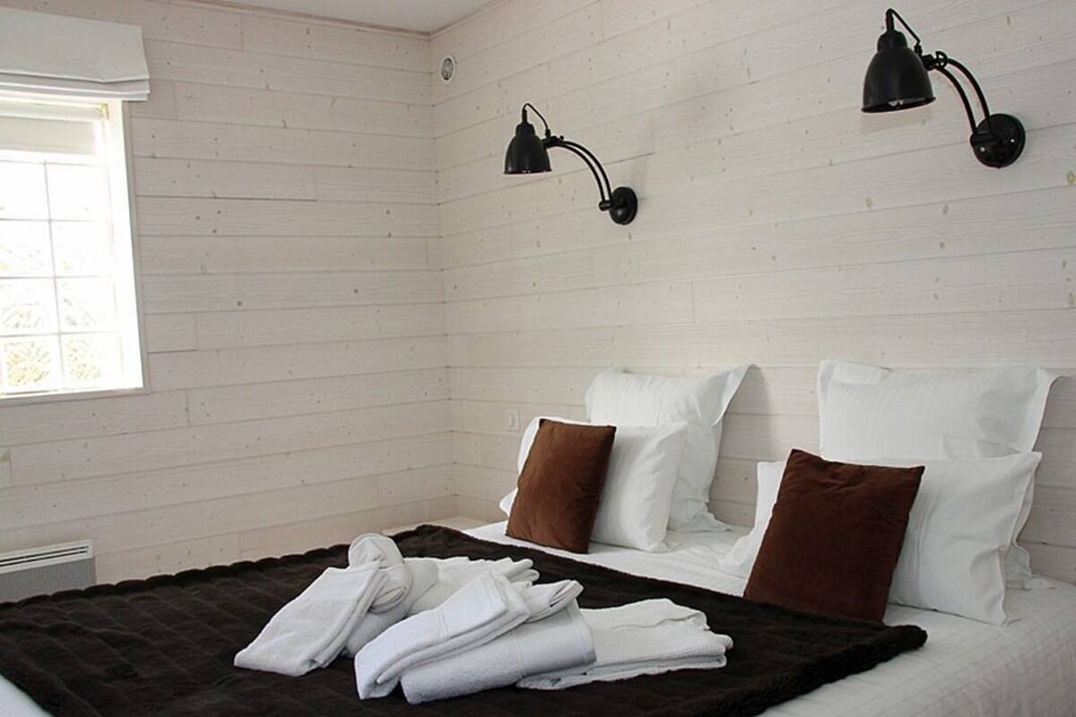 A bedroom with a bed, white and brown pillows, a black throw blanket, and two wall-mounted lamps.