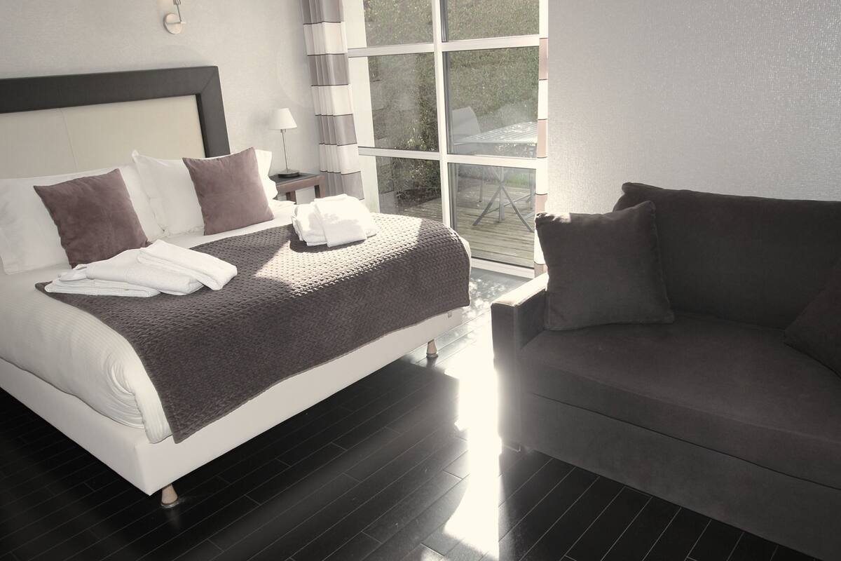 A modern hotel room with a bed, a sofa, a window, and a nightstand.