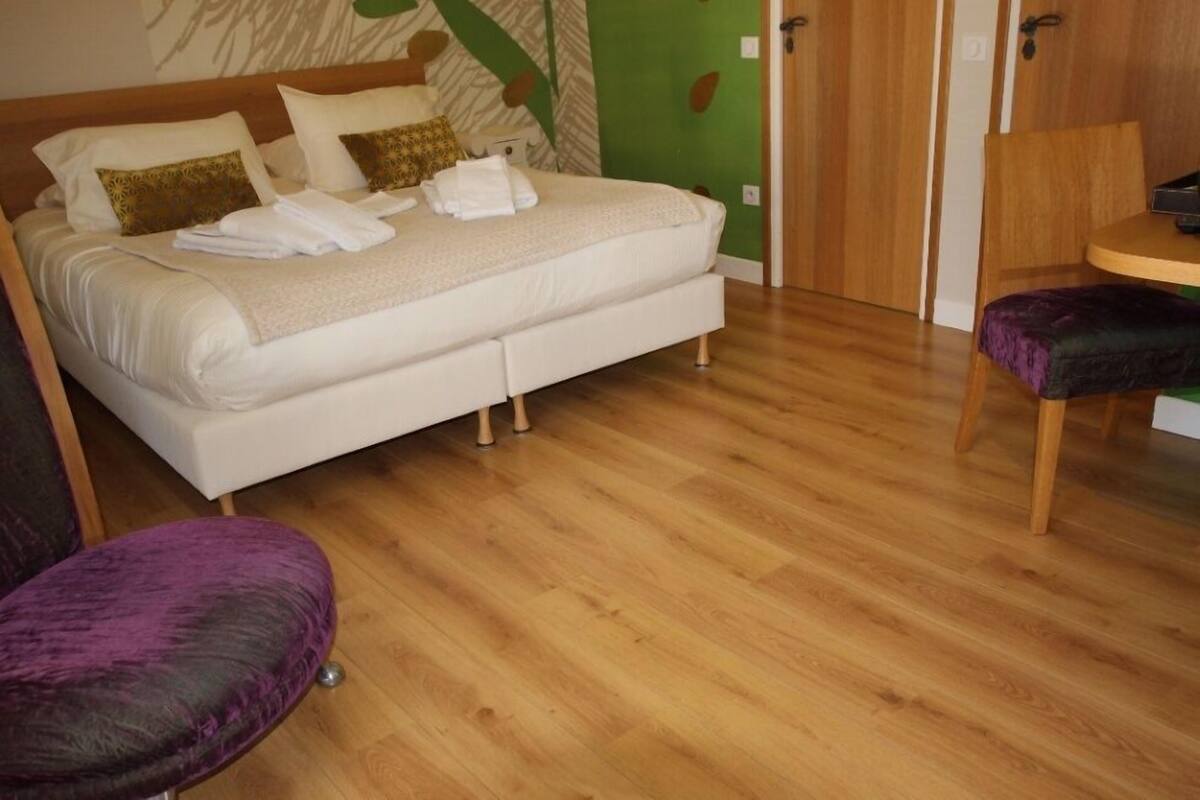 A neatly made bed with pillows and towels, a wooden floor, a purple chair, and a small table.