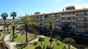 Ein mehrstöckiges Hotel mit Balkonen, Palmen und einem Schwimmbad.
