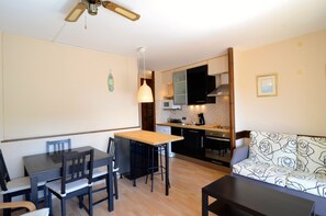 A compact kitchen with a dining area, a ceiling fan, and a sofa with a patterned cover.