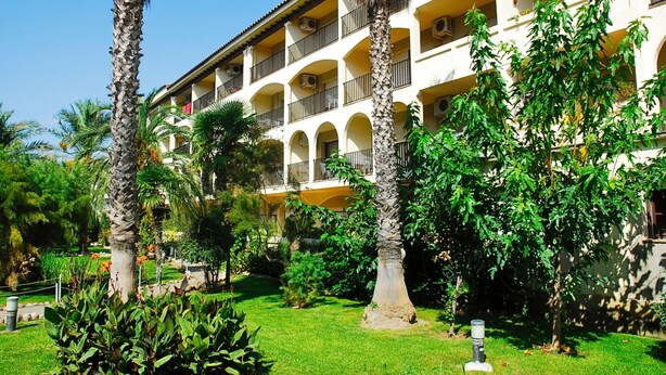 Ein mehrstöckiges Hotel mit Balkonen, umgeben von üppiger Vegetation und Palmen.