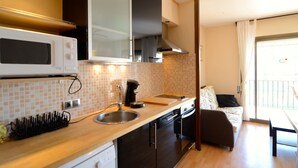 Eine kompakte Küche mit Mikrowelle, Spüle und Kaffeemaschine, ein kleiner Essbereich mit Tisch und Stuhl sowie ein Balkon mit Geländer.