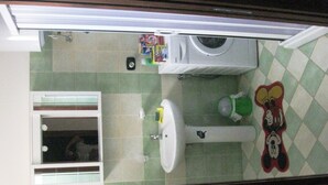 A small bathroom with a sink, mirror, green-tiled walls, a washing machine, and a Mickey Mouse rug.
