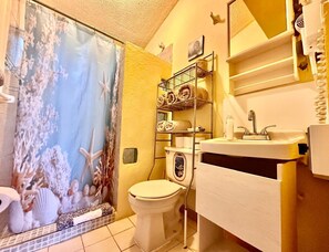 Une salle de bain équipée d’un rideau de douche orné d’une scène marine, de toilettes, d’un lavabo avec un miroir et d’un porte-serviettes.