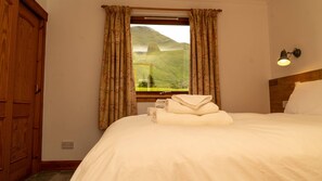 A hotel room with a bed, a window with curtains, a wooden door, and a wall-mounted light fixture. - Kingfisher a beautiful 5 star, 2 bedroom, 2 bathroom holiday property that can sleep up to 4 people (Crianlarich)