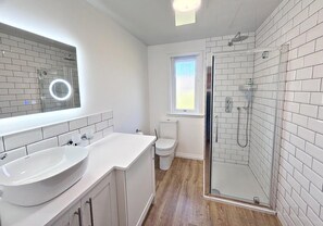 A bathroom with a large white sink, a toilet, a shower with a glass door, and a window. - Kingfisher a beautiful 5 star, 2 bedroom, 2 bathroom holiday property that can sleep up to 4 people (Crianlarich)