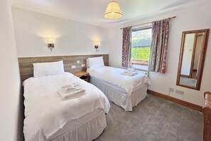 A hotel room with two beds, a window with curtains, a mirror, and a lamp. - Kingfisher a beautiful 5 star, 2 bedroom, 2 bathroom holiday property that can sleep up to 4 people (Crianlarich)