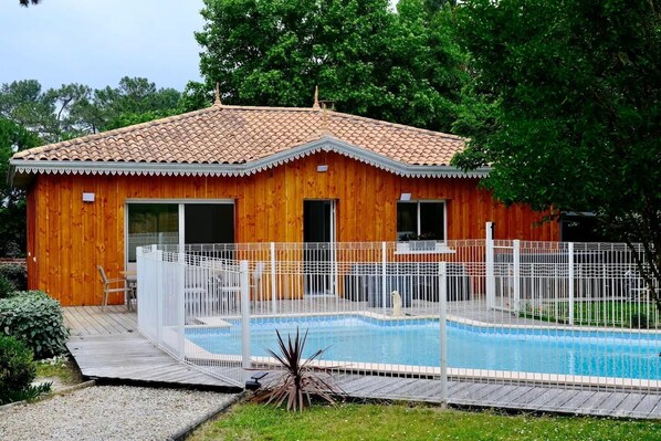 A wooden house with a tiled roof, a swimming pool, and a fenced deck area.