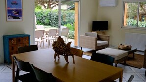 Un comedor con una mesa, sillas, un sofá de mimbre, un televisor y vistas al exterior.