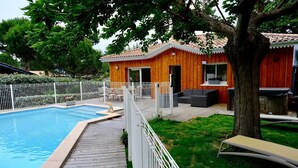 Un patio trasero con piscina, terraza de madera y zona de estar al aire libre.