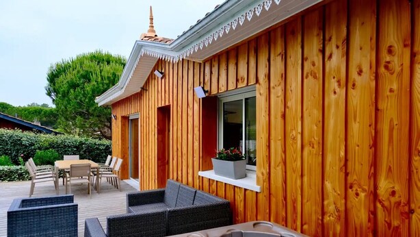 Una cabaña de madera con jacuzzi, mobiliario exterior y una ventana con planta.