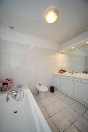 A modern bathroom with a bathtub, a sink, a bidet, and a large mirror.