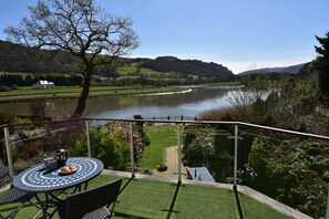 A terrace with a table and chairs, overlooking a river and hills. - Charming River Conwy Retreat with Stunning Views (Tal-y-cafn)