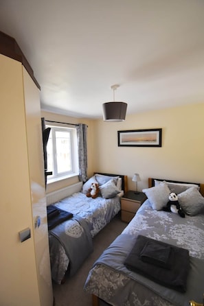 A bedroom with two single beds, a window with curtains, a framed picture on the wall, and a hanging light fixture. - Charming River Conwy Retreat with Stunning Views (Tal-y-cafn)