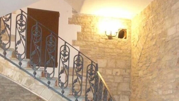 A grand staircase with ornate metal railings leading to a landing with a stone fireplace and a vase of flowers. - B&B Savarini (Palo del Colle)