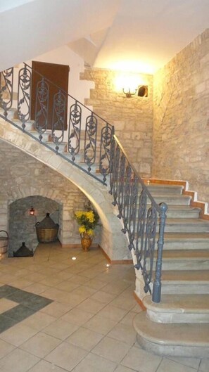 A grand staircase with ornate metal railings leading to a landing with a stone fireplace and a vase of flowers. - B&B Savarini (Palo del Colle)