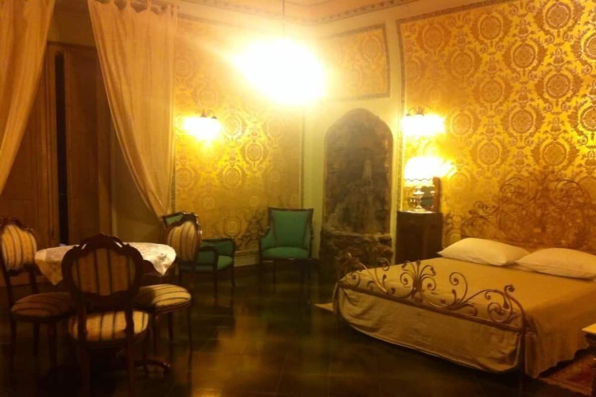 A hotel room with a bed, two chairs, a table, and two wall-mounted lamps.