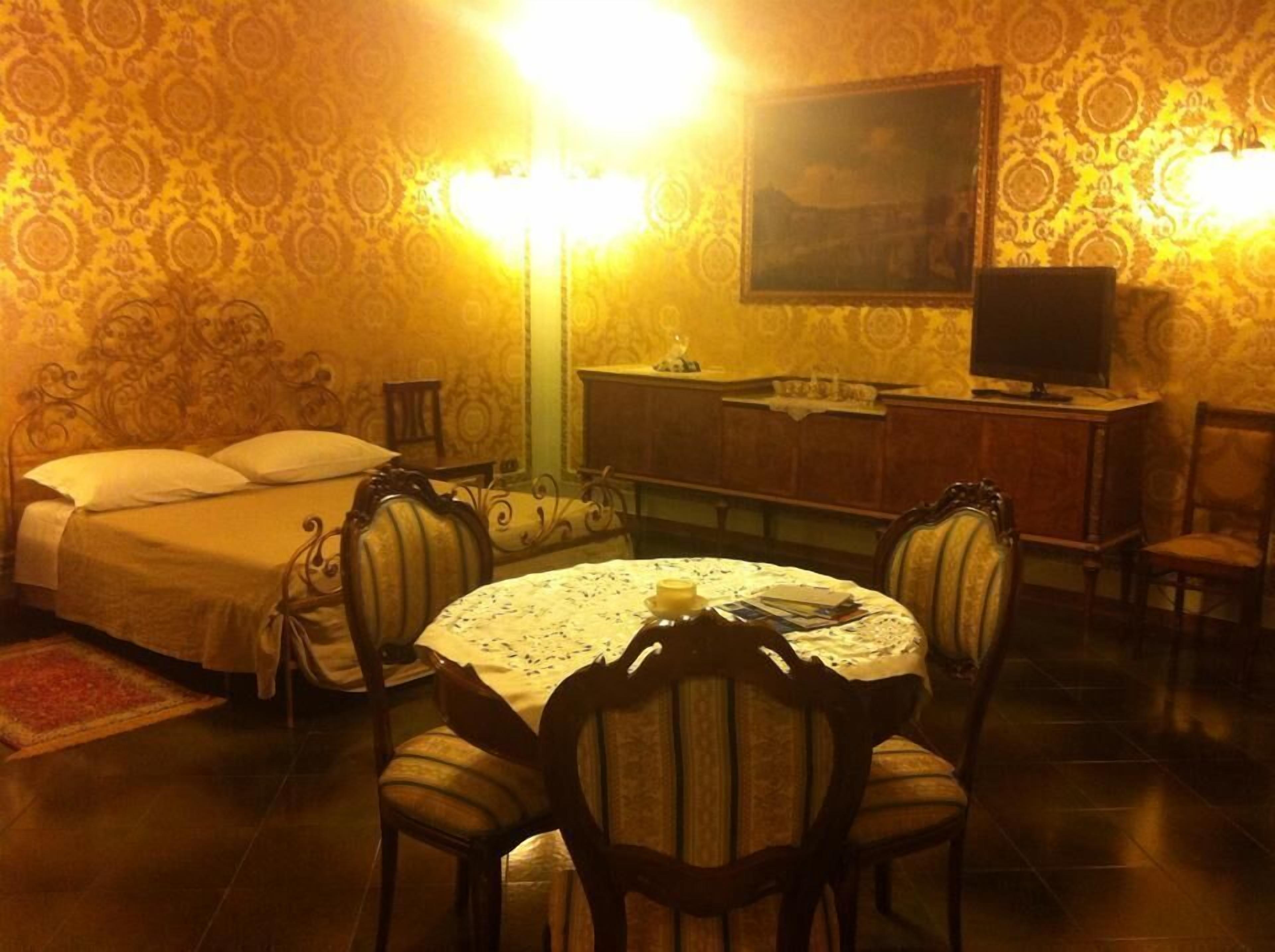 A room with a bed, a round table with chairs, a television, and a cabinet.