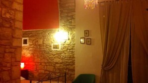 A room with stone walls, a chandelier, a green chair, and a red accent wall. - B&B Savarini (Palo del Colle)