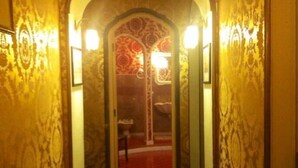A hallway with patterned wallpaper, a tiled floor, and a doorway leading to a room with a red carpet. - B&B Savarini (Palo del Colle)