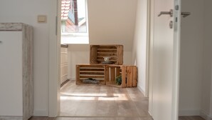 A hallway with wooden crates and a small table, leading to a room with a window and a door.