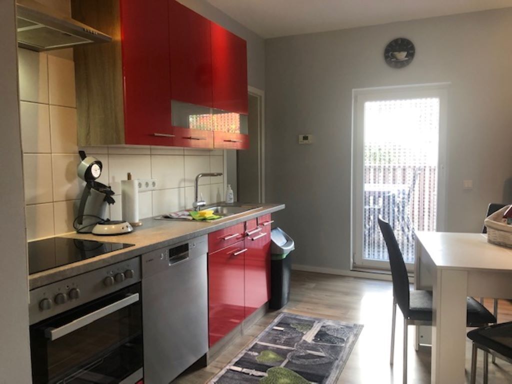 A modern kitchen with red cabinets, a dishwasher, and a stove. There is a dining area with a table and chairs.