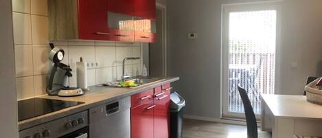 A modern kitchen with red cabinets, a dishwasher, and a stove. There is a dining area with a table and chairs.