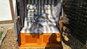 A wooden bench with striped cushions and a floral pillow, placed outdoors on mulch.