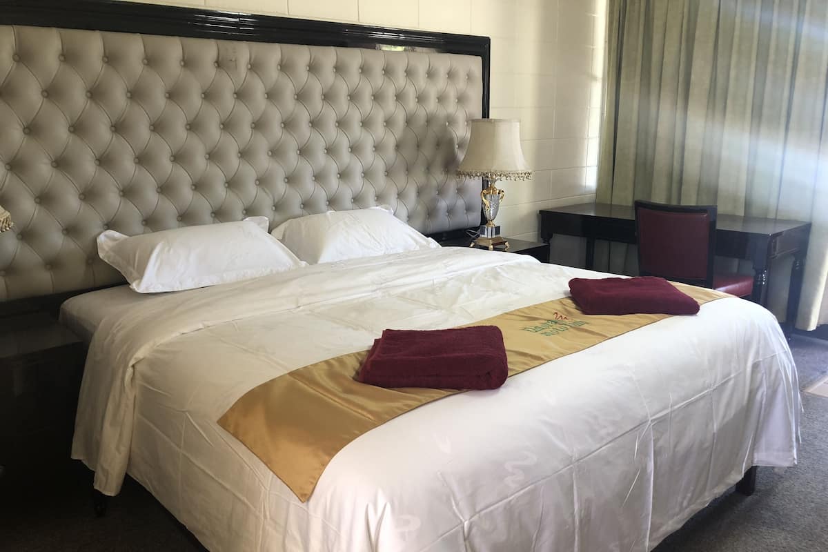 A hotel room with a large bed, a headboard, a bedside table, a lamp, and a chair.