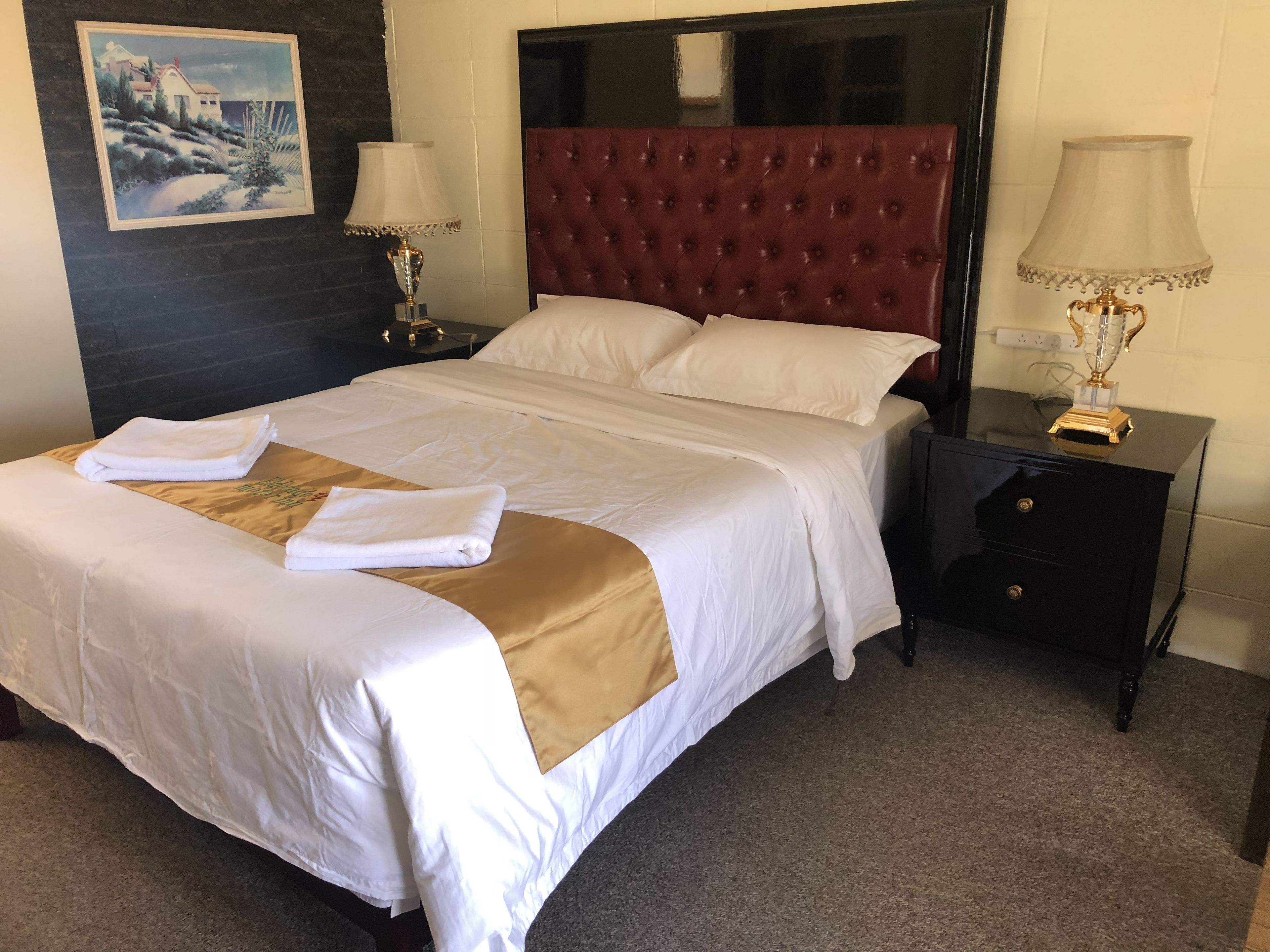 A neatly made bed with white and gold linens, a red tufted headboard, and two bedside lamps.