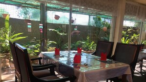 A restaurant with a glass table and chairs, surrounded by greenery and a view of the outdoors. - Inland Oasis Motel (Soldiers Hill)