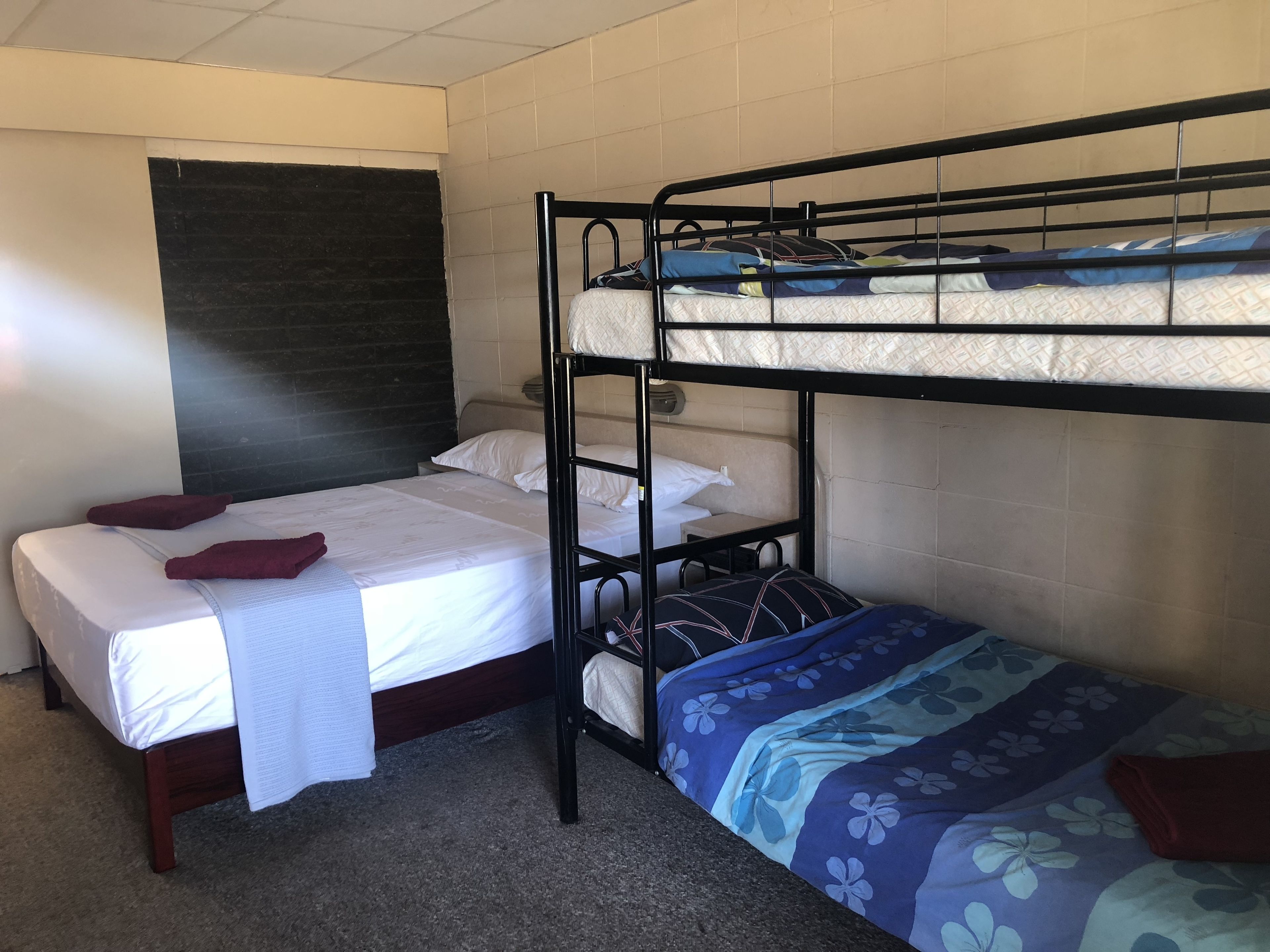 Quarto com beliche de madeira, sendo a cama de baixo com colcha florida e cabeceira encostada em parede revestida de azulejos.