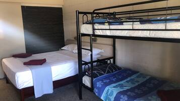 Quarto com beliche de madeira, sendo a cama de baixo com colcha florida e cabeceira encostada em parede revestida de azulejos.