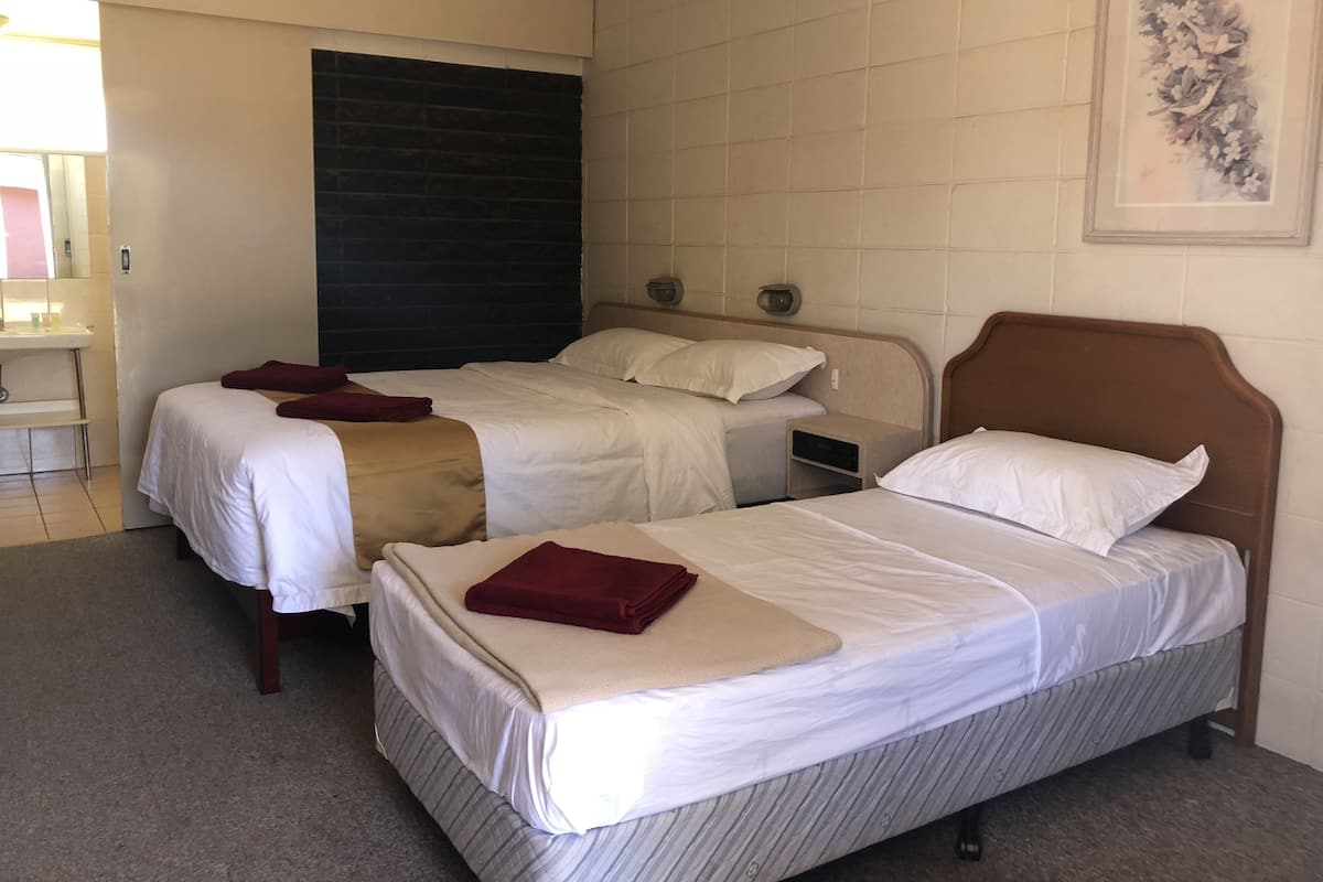 A hotel room with two beds, a bedside table, a small desk, and a bathroom.