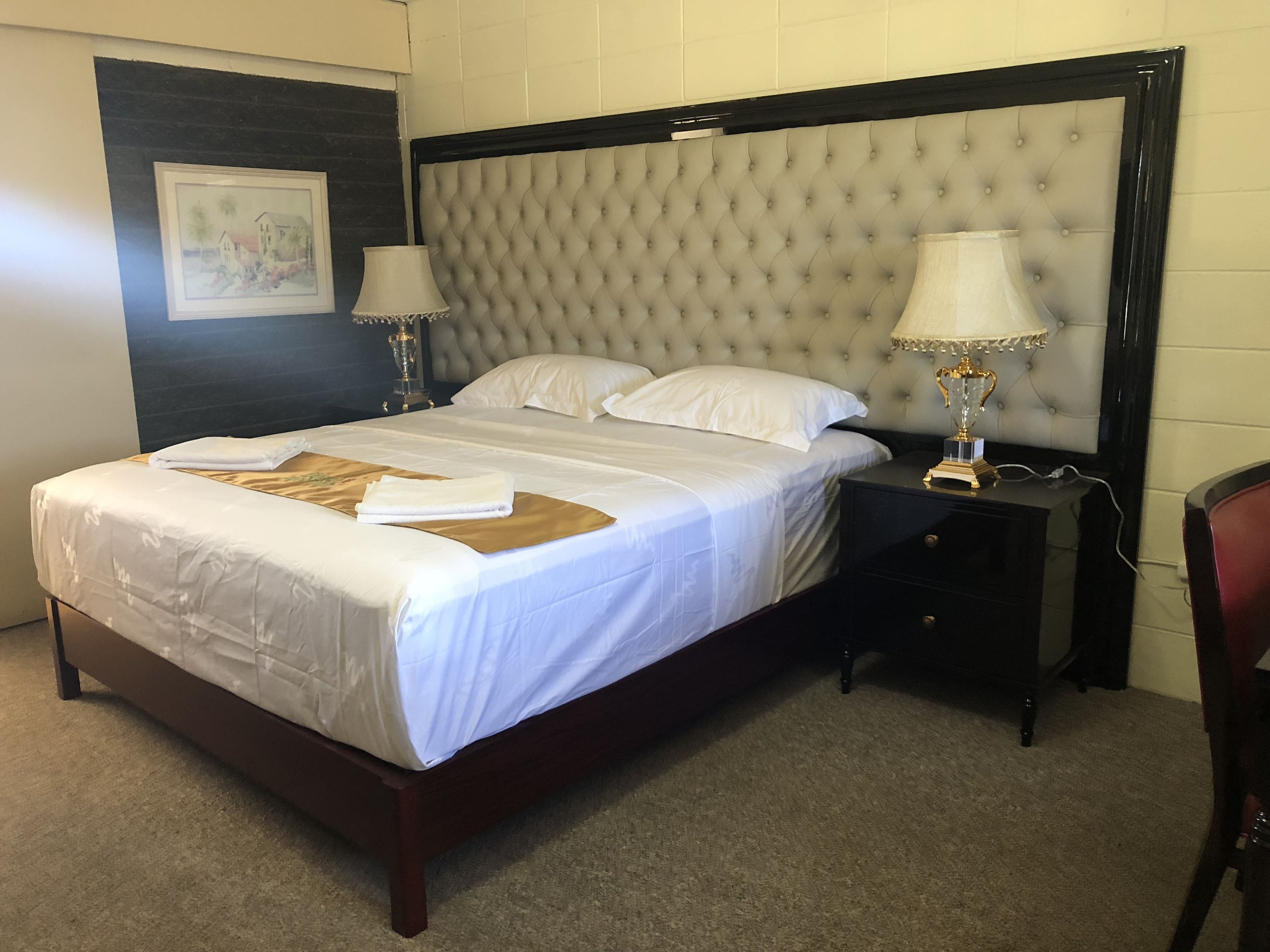 A neatly made bed with white linens and a brown throw, a tufted headboard, two bedside lamps, and a small nightstand with a lamp.
