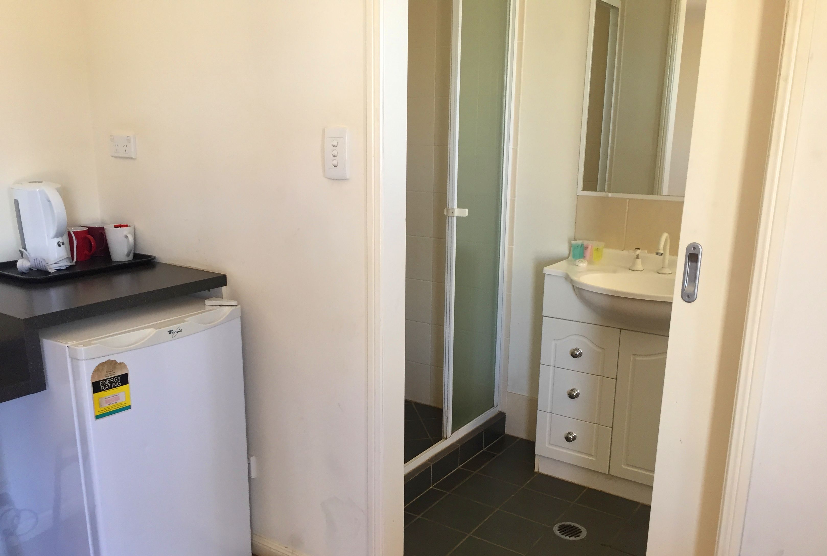 Un baño pequeño con un lavamanos blanco, espejo y ducha con puerta de cristal.