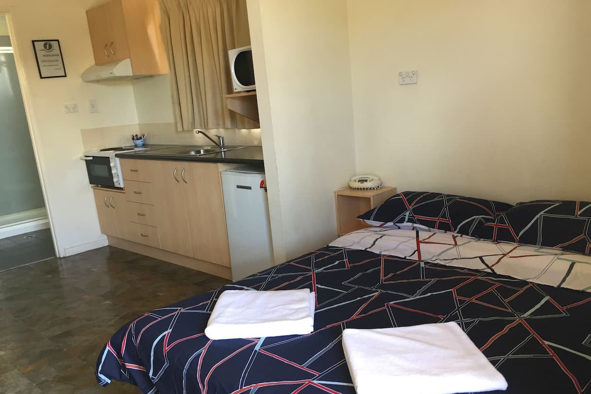 A compact room with a bed, a small kitchenette, and a bedside table with a phone.