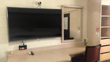 A hotel room with a flat-screen TV mounted on the wall, a desk with a chair, and a mirror.