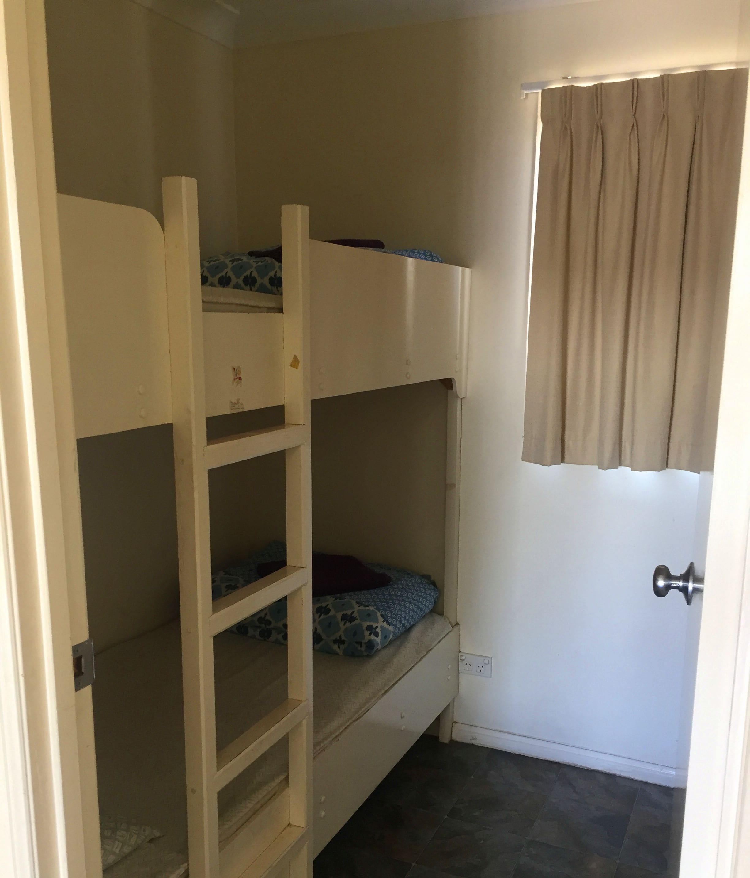 Habitación con literas, una escalera, una ventana con cortinas y una puerta.