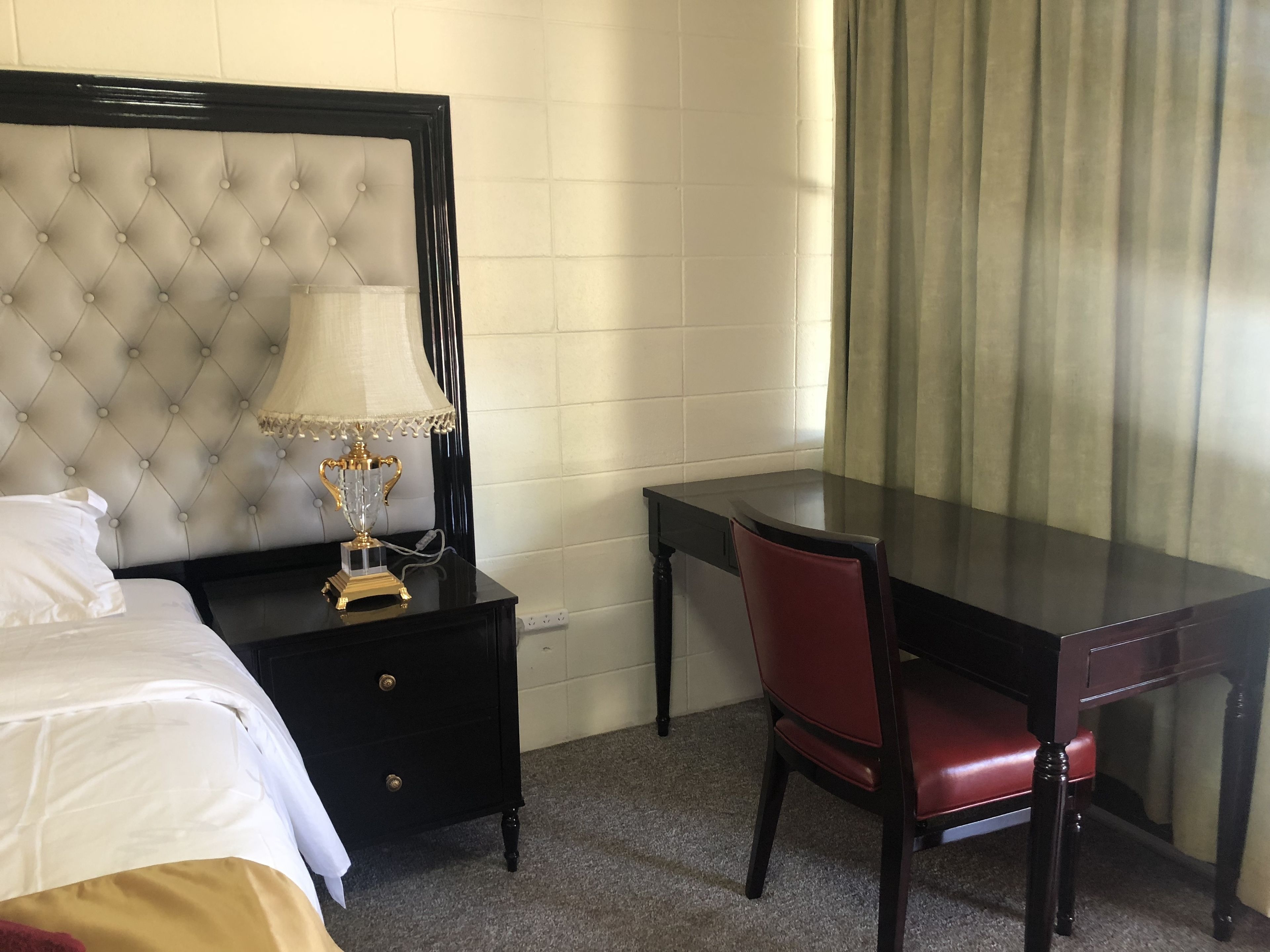 A hotel room with a bed, a bedside table with a lamp, a desk, and a chair.