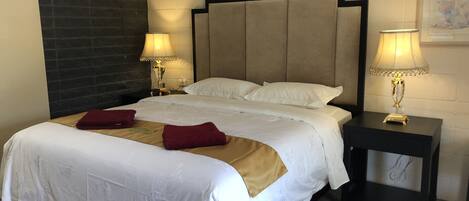 A hotel room with a large bed, two bedside lamps, a nightstand, and a dark wall with a textured pattern.