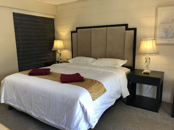 A hotel room with a large bed, two bedside lamps, a nightstand, and a dark wall with a textured pattern.