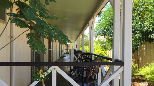 A covered porch with a wooden deck, white railings, and outdoor furniture. - Inland Oasis Motel (Soldiers Hill)