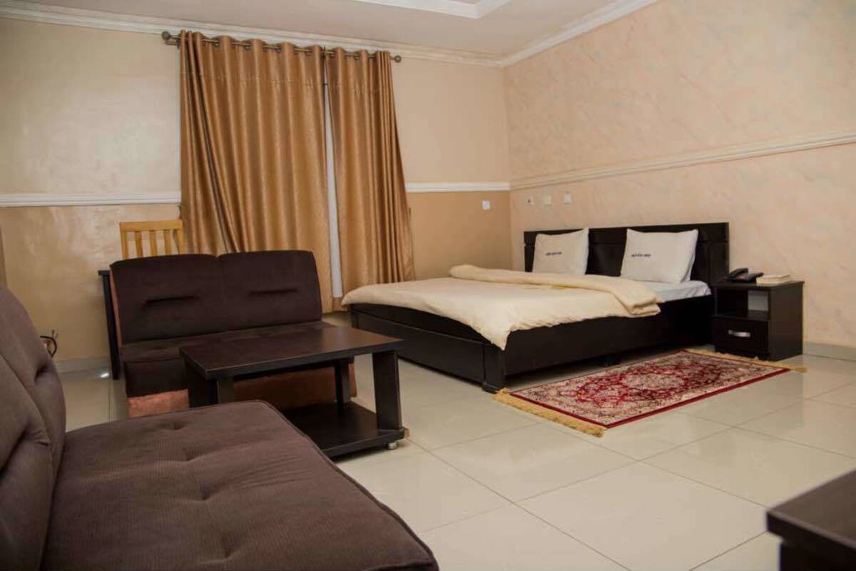 A hotel room with a bed, a sofa, a small table, a nightstand, and a red and white patterned rug.