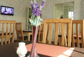 Un comedor con sillas de madera y una mesa, un jarrón con flores, y un televisor en la pared.