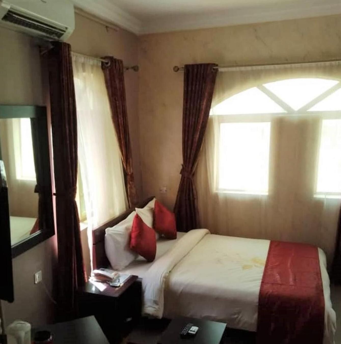 A hotel room with a bed, a nightstand, a mirror, and a window with curtains.