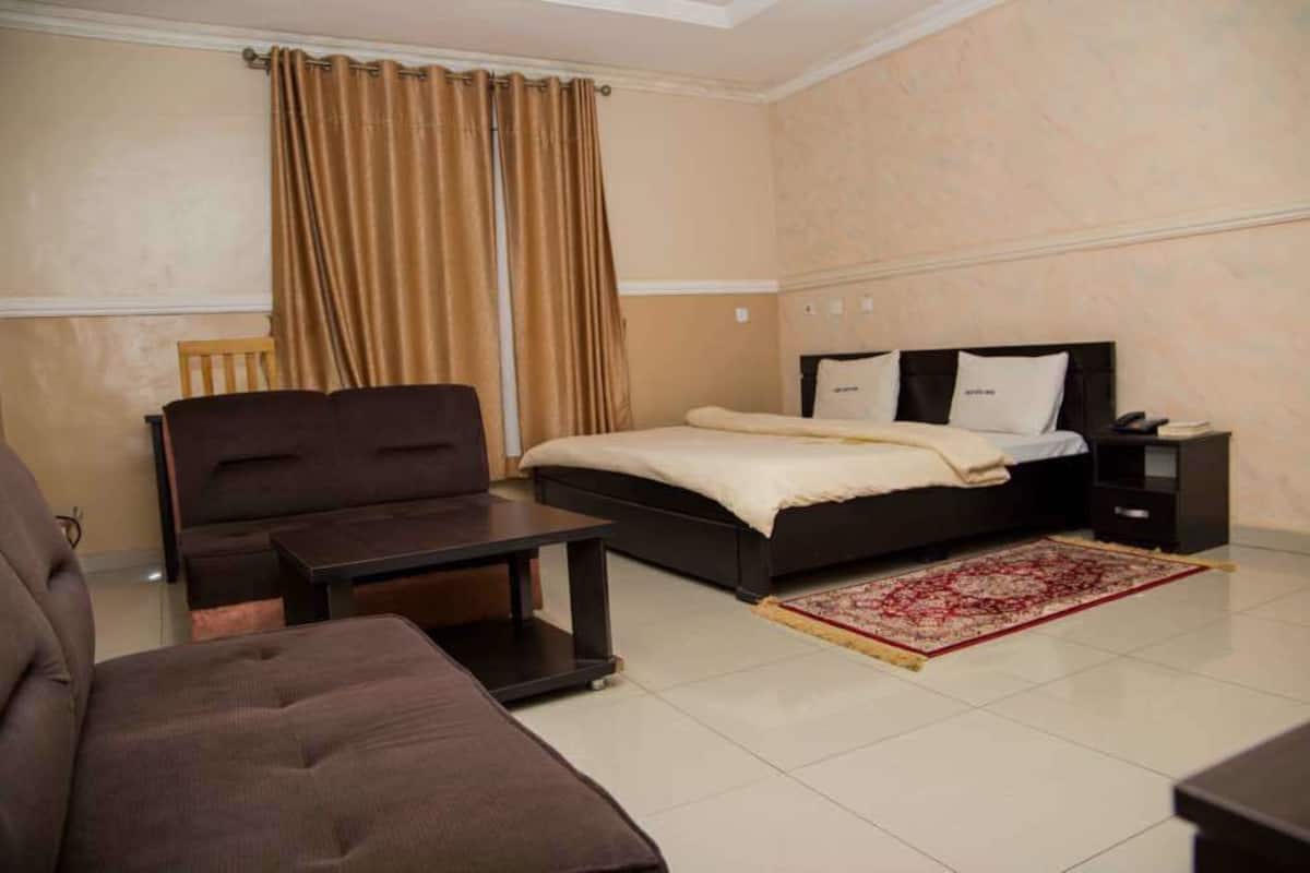 A bedroom with a bed, a sofa, a nightstand, and a table.