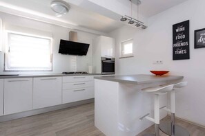 Een moderne keuken met witte kastjes, een inbouwoven en een groot kookeiland met barkrukken.