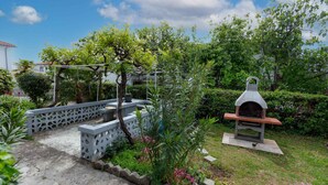 Un jardin avec un espace barbecue, une pergola et une clôture blanche.